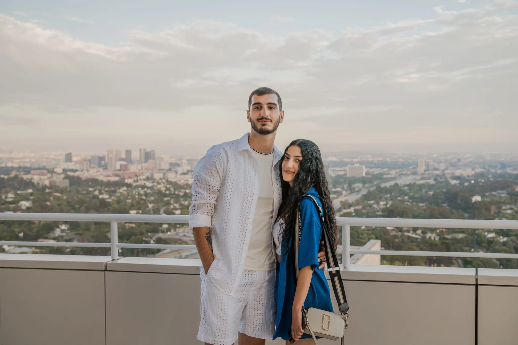 Couple in white and blue on a rooftop terrace, Los Angeles sprawling to the horizon behind them