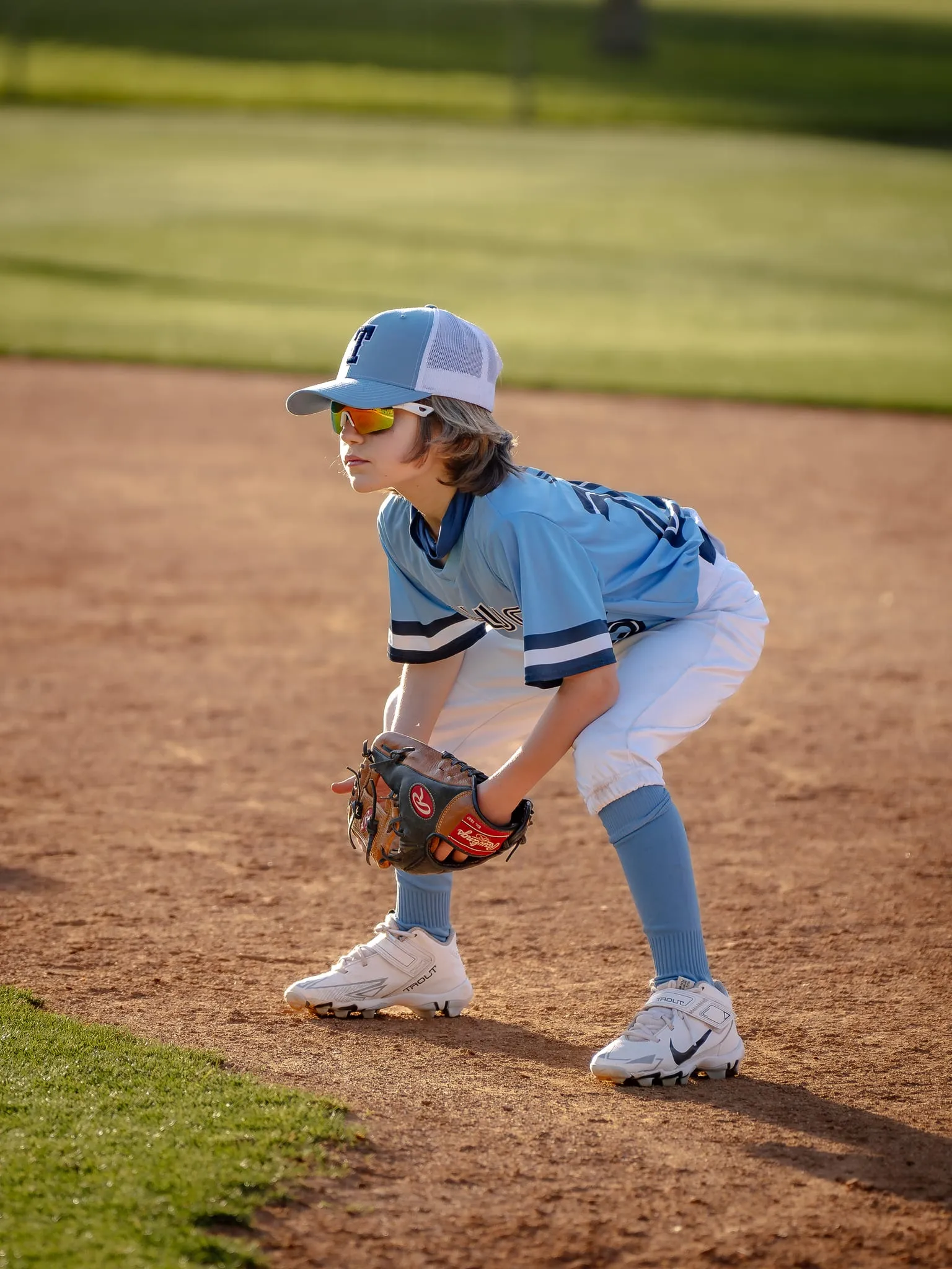 Young infielder crouched low in golden evening light, glove down, eyes on the plate