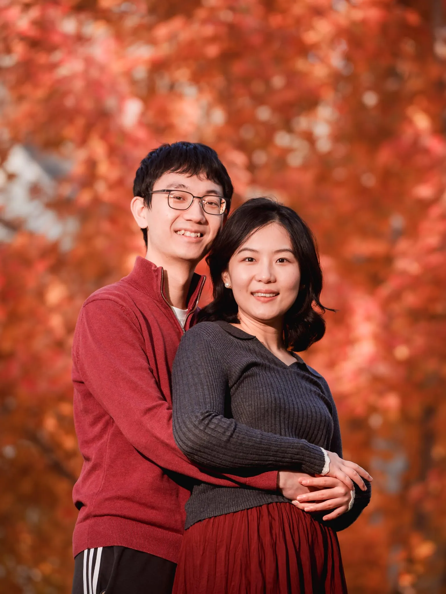 Couple portrait session in the Bay Area — a smiling couple embraces beneath brilliant red maple leaves in warm golden-hour light