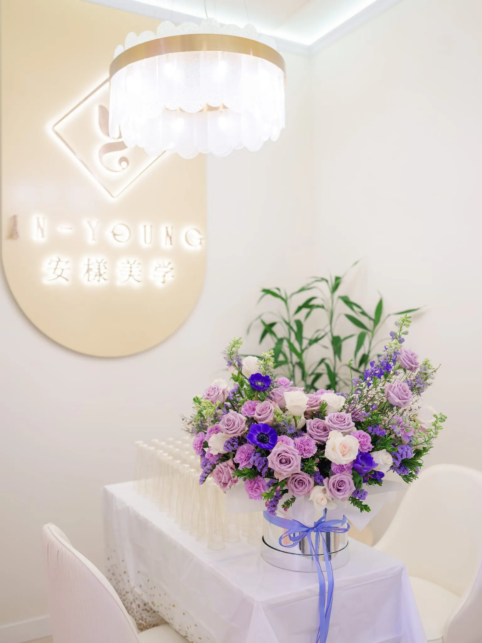 Logo wall, crystal chandelier, and a lavender bouquet styled in a San Jose beauty studio interior